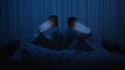 A couple sits back to back in bed at night using smartphones