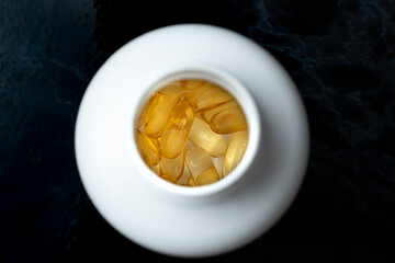 Top view of bottle with bright orange yellow omega 3 capsule pills on black marble kitchen table.