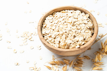 Rolled oats in wooden bowl with golden ears on white background.