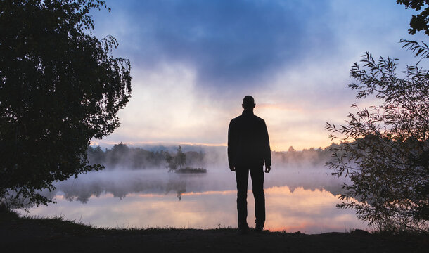 Man standing on pond shore at morning in blue hour. Calm Czech landscape background