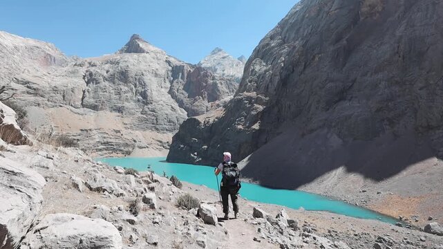 Big Allo lake view with mountain range and turquoise water and a small hiker's silhouette in Fann mountains Pamir Alay Tajikistan