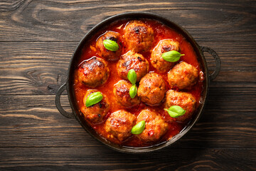 Meatballs in tomato sauce with basil leaves on wooden table.