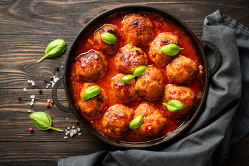 Meatballs in tomato sauce with basil leaves on wooden table.
