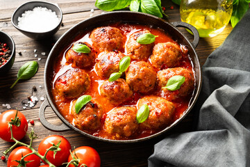 Meatballs in tomato sauce with basil leaves on wooden table.