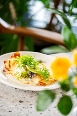 Gourmet crepe topped with fresh frisée and arugula, drizzled with orange sauce, served on a terrazzo surface with blurred floral background. Elegant restaurant-style plating