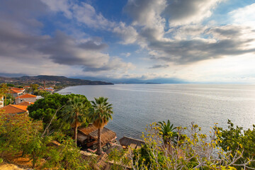 Widok na nadmorskie miasto Molivos, domy z palmami i morze pod zachmurzonym niebem na greckiej wyspie Lesbos © anettastar