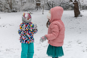 Two little girls playing games and having fun, having a snow ball fight in the snow. Happy children play snowballs