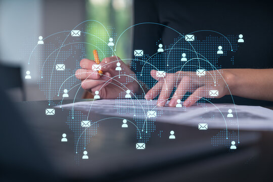 Global email communication network concept with digital user icons and message symbols overlaying hands writing on documents at a desk in office environment.