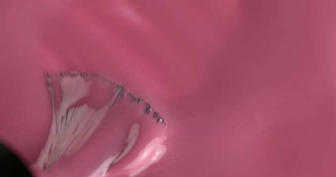 Liquid nail polish surface, pink nail polish is applied with a brush manicure concept, slow motion. Manicure salon, nail polish texture, background. Top view.