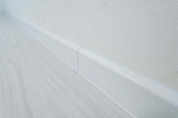 This image features a detailed closeup of a white skirting board that is positioned against a...