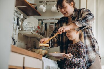 Mother and daughter cooking pancakes together in kitchen