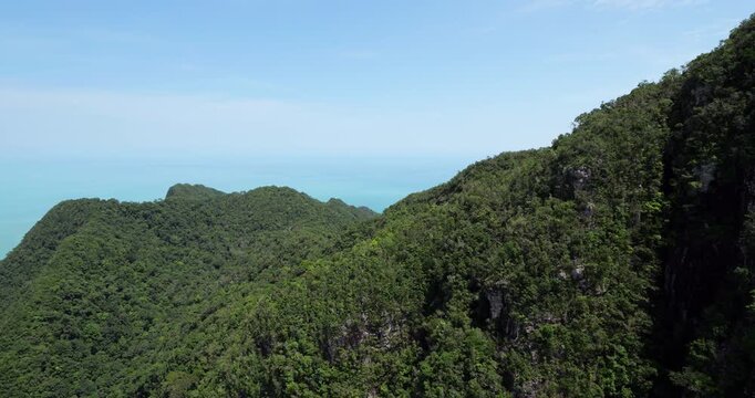 Lush green rainforest covering steep slopes of island mountains, aerial view from descending cable car. Ancient Cambrian rock formations of Mat Chinchang Geopark, among the oldest in Southeast Asia.