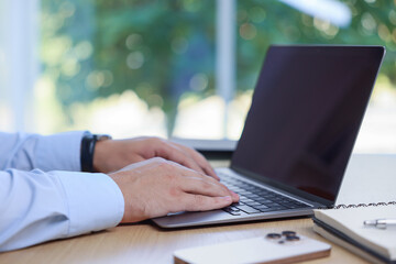 Man working on laptop at wooden table indoors, closeup