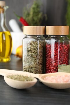 Different spices and glass jars on grey wooden table, closeup