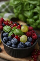 Different ripe juicy berries and basil in bowl on wooden table, closeup