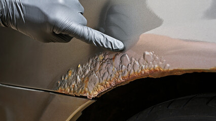 Close-up of a gloved hand inspecting rust damage and peeling paint on a car surface. Concept for vehicle inspection, damage assessment, insurance claims and corrosion diagnostics.