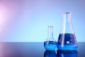 Glass flasks with blue liquid on mirror surface against color background, space for text