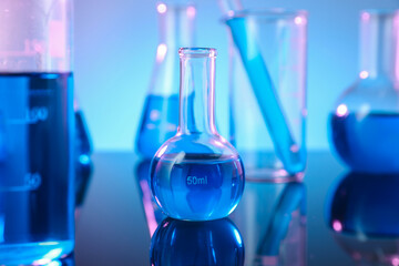 Different glassware with blue liquid on mirror surface against color background