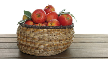 Fresh apples in wicker basket and green leaves on wooden table against white background