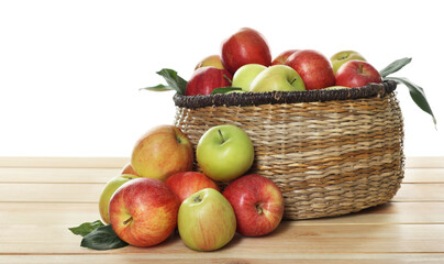 Fresh apples in wicker basket and green leaves on wooden table against white background