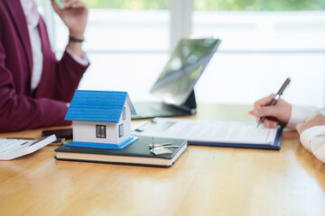 Business people discussing and signing real estate contract with miniature house model on desk,...