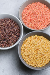 Three bowls filled with colorful lentils, showcasing a variety of textures and hues, arranged on a textured surface, emphasizing healthy food choices and culinary diversity