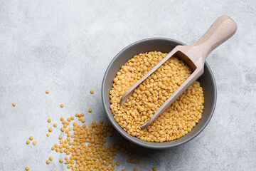 Yellow lentils in a gray bowl with a wooden scoop, scattered lentils on a textured surface, showcasing healthy ingredients for cooking and nutrition