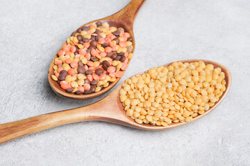 Colorful assortment of lentils displayed in wooden spoons on a textured surface, showcasing diverse varieties and natural hues, emphasizing healthy food choices and nutrition