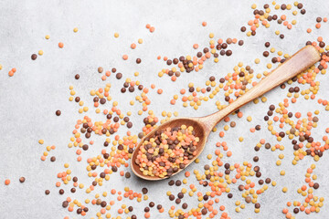 Colorful lentils grains scattered on a light gray surface, with filloed wooden spoon