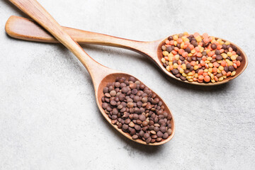 Wooden spoons filled with colorful lentils, showcasing a variety of textures and hues, arranged on a light concrete surface, emphasizing healthy food choices and culinary creativity