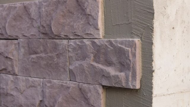Wall prepared for decorative stone cladding with the first tiles already installed. Close-up view of the facade before full masonry work and exterior renovation.