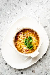 Traditional French onion soup in a white bowl, topped with melted cheese and parsley, served on a plate with napkin. Rustic presentation on light speckled background