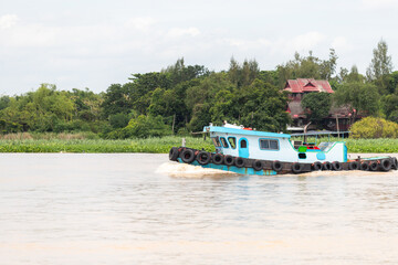 blue river tugboat cruising with black tire fenders near green riverbank and traditional house