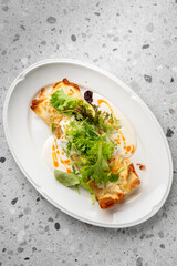 Gourmet baked crepes stuffed and topped with creamy white sauce, orange oil drizzle, and fresh greens. Elegant restaurant-style plating on a white oval dish.