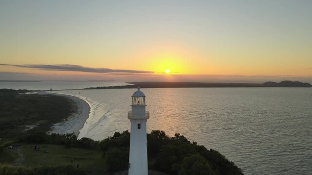 Vista a&eacute;rea com drone do far&oacute;l da conchas da Ilha do Mel em Paranagu&aacute; no litoral do Paran&aacute; com oceano atl&acirc;ntico ao p&ocirc;r-do-sol alaranjado