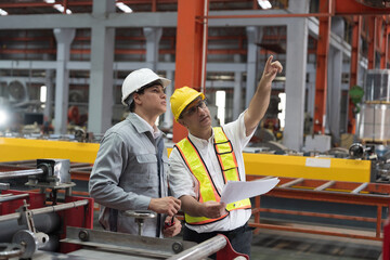 Supervisor and male engineer working together in factory. Conveyor blet in prouduction line during manufacturing process. Factory worker at work, discussing of work, wearing safety uniform