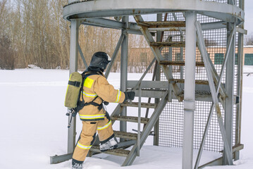 A firefighter in a helmet and protective clothing, with a breathing apparatus, climbs the stairs. In winter, firefighters conduct outdoor training. The rescue service.