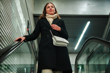 A determined young woman rides the escalator with confidence, looking ahead as she navigates...