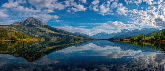 Serene lake reflects majestic mountain range under vast, partly cloudy sky, creating tranquil and picturesque landscape