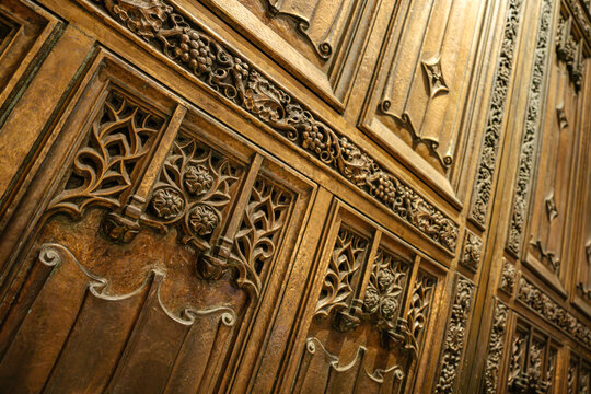 This angled image shows the detailed bronze door of St. Patrick's Cathedral in New York City. Gothic carvings of flowers, vines, and grape clusters decorate the richly textured surface.
