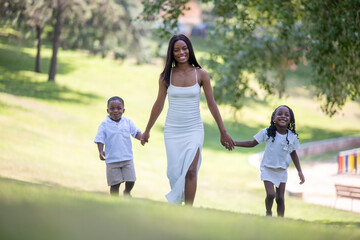 Fototapeta premium Woman in elegant white dress walking hand in hand with two children in park