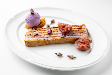 Gourmet plated dessert with layered pastry, purple cream, fig, flower garnish, and berry ice cream on crumb base. Elegant presentation on white dish, fine dining concept.