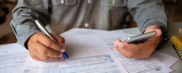 Budget and Tax planning concept, Accountant Hand is calculating company annual tax. Man holding smartphone. Personal income tax form for income under US law, season to paying tax-banner image.