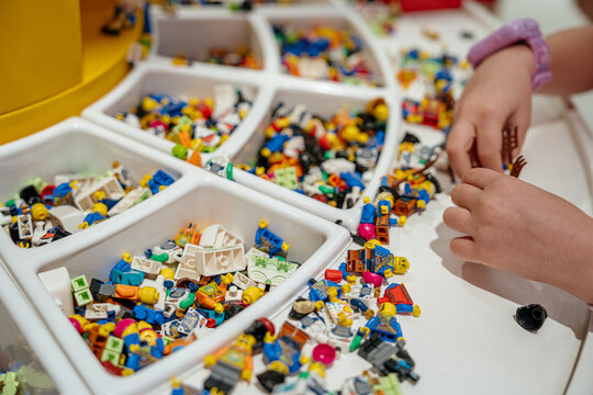 New York City, New York, USA - 07.31.2024: A childs hands are building a LEGO mini figure using colorful parts from sorting trays. The table is filled with small LEGO heads, bodies, and accessories
