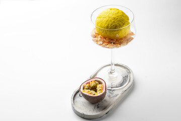 Creative food styling with lemon in wine glass filled with sliced almonds, passion fruit half on marble tray. Minimalist gourmet concept with vibrant tropical accents.