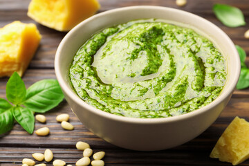 Fresh pesto sauce in bowl and ingredients on wooden table, closeup