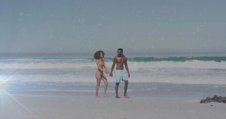 Walking couple holding hands along shoreline beach, wearing orange bikini, blue trunks with flare