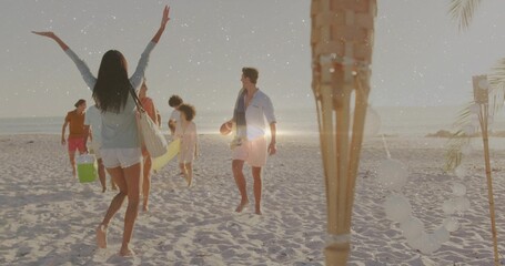 Waving beachgoer wearing white shorts greeting friends on sandy beach with surfboard and lanterns