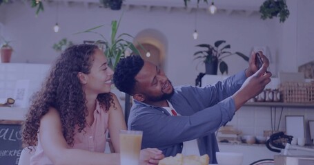 Leaning couple sharing smartphone at wooden countertop in cafe, with latte, croissants, plants