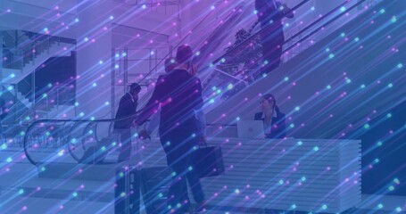 Walking Asian man pulling suitcase and carrying briefcase in corporate lobby, with escalator